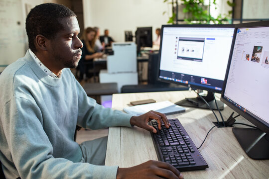Focused office worker using dual monitors in modern open office