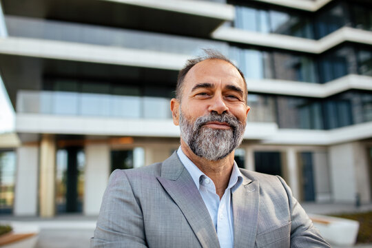 Confident bearded businessman smiling outside modern office building in city