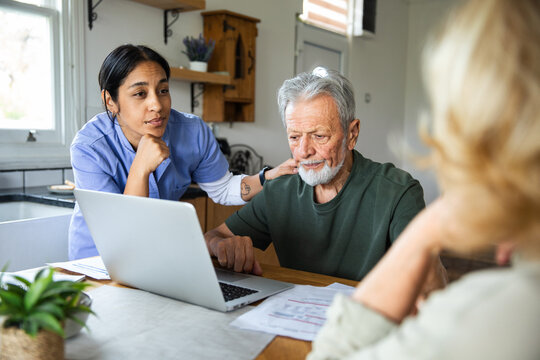 Caregiver helping senior couple review bills on a laptop at home