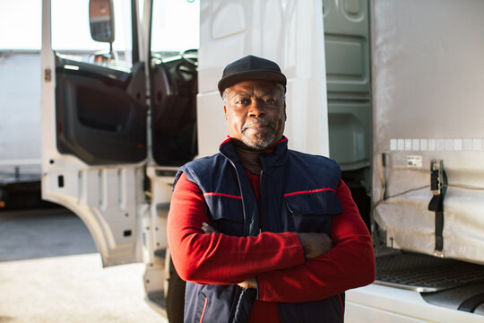 Confident truck driver standing by semi truck in logistics yard