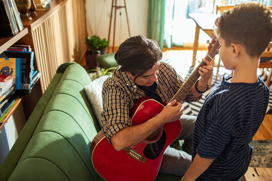 Father teaching son acoustic guitar at home