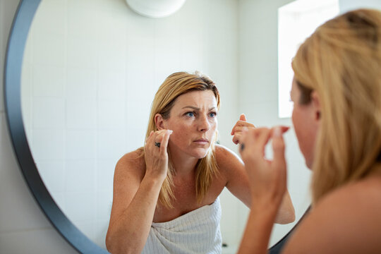 Woman examining skin in bathroom mirror at home