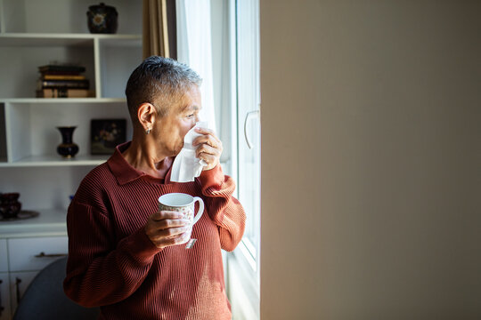 Senior man with cold drinking tea at home by window