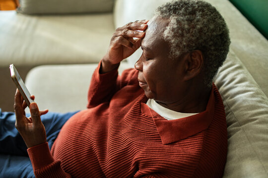 Older man worried on sofa checking smartphone at home