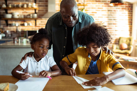 Grandfather helping children with schoolwork at kitchen table