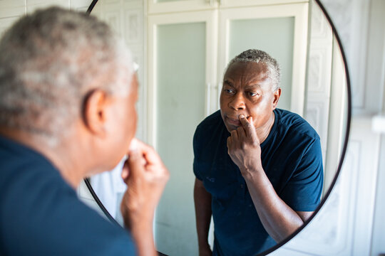 Senior man examining his face in bathroom mirror at home