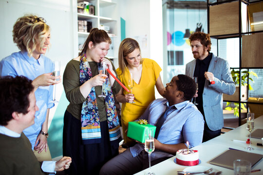 Diverse coworkers celebrate birthday with cake in modern office