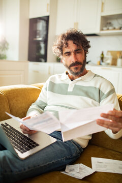 Middle-aged man reviewing bills at home on sofa