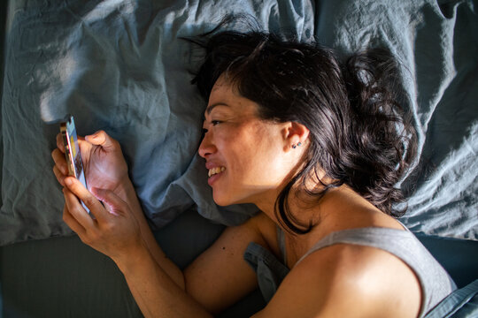 Smiling woman in bed using smartphone at home