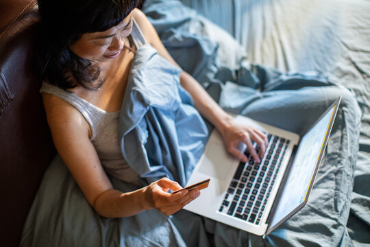 Woman shopping online with credit card on laptop in bed at home
