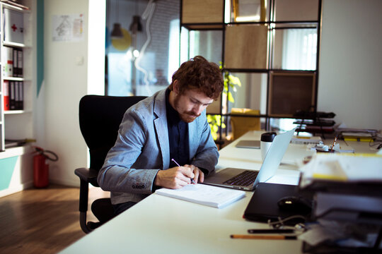 Young professional writing notes at laptop in modern office