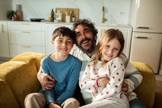 Father with son and daughter relaxing on sofa in home kitchen