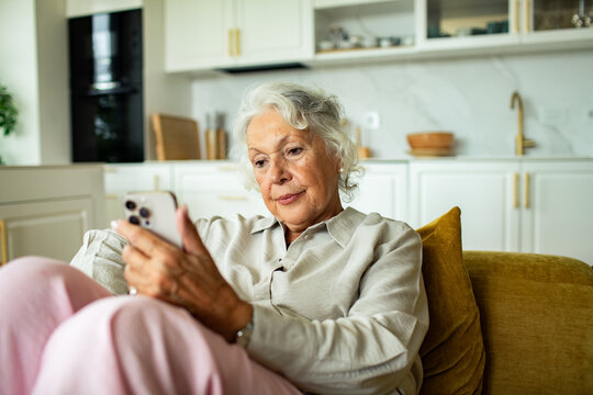 Senior woman using smartphone on sofa in home kitchen