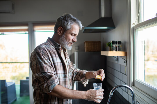 Mature man squeezing lemon into water in home kitchen