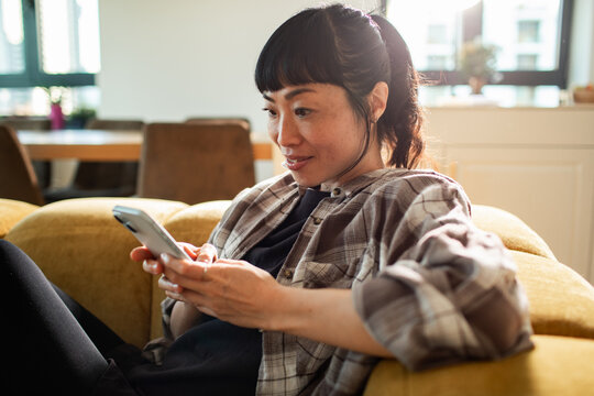 Relaxed woman using smartphone on sofa at home