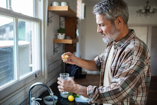 Mature man squeezing lemon into water in home kitchen