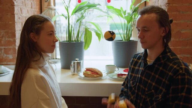 Close up of two people conversing at table with food and drink. man juggles small objects while interacting set against indoor backdrop featuring brick walls plants natural light soft