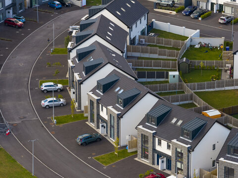 Aerial view of a modern residential housing development featuring terraced houses with dark grey roofs, stone cladding, and private gardens in Donegal, County Donegal, Ireland.