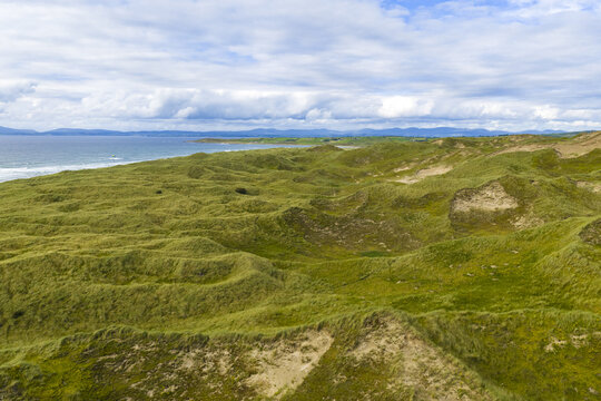 Aerial view of Finner sand dunes featuring rolling green hills, sandy patches, and the coastline of the Atlantic Ocean in County Donegal, Ireland.