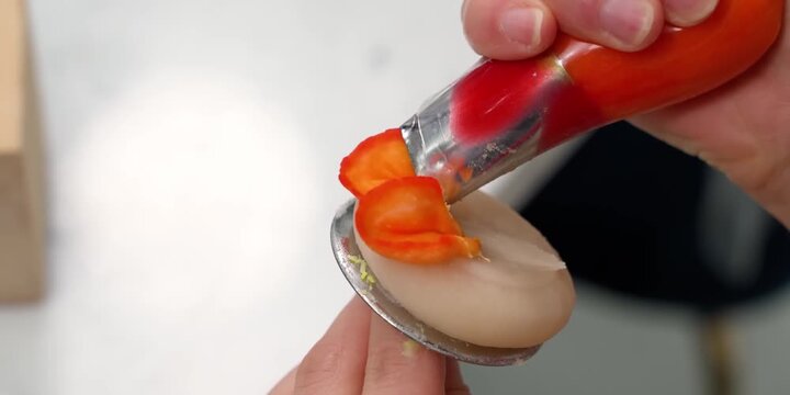 A detailed close-up shot capturing a pastry chef skillfully piping vibrant orange and red two-tone buttercream petals onto a metal flower nail. Using a specialized petal tip, the decorator carefully l