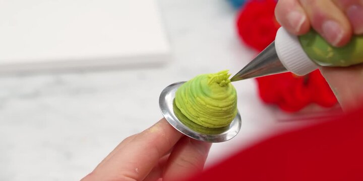 A close-up, high-definition shot captures a pastry chef or baker carefully piping realistic green buttercream frosting onto a stainless steel flower nail to create an edible cactus succulent. Using a 