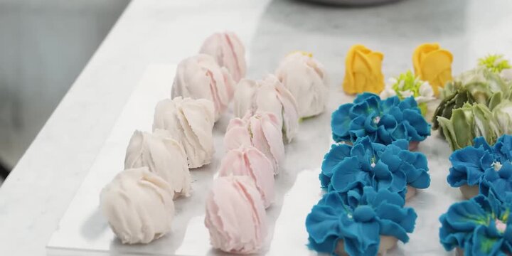 A high-angle panning shot showcasing rows of intricately decorated cupcakes topped with colorful buttercream flowers. The display features vibrant blue and deep red floral piping patterns, with soft y