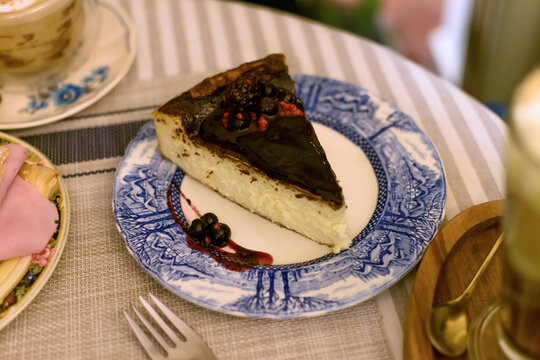 Deliciosa porci&oacute;n de tarta de queso cubierta con mermelada y frutos rojos frescos servida en un plato vintage azul y blanco en una cafeter&iacute;a.