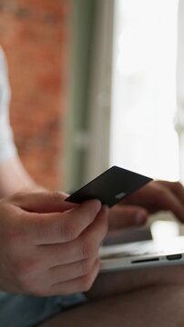 Young man shops online with credit card and phone while relaxing in bedroom during daytime. Vertical video