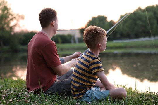 Father and his little son fishing together near river outdoors
