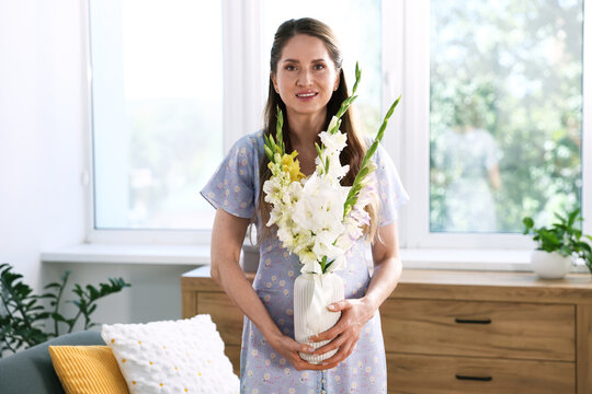 Woman with beautiful gladiolus flowers at home