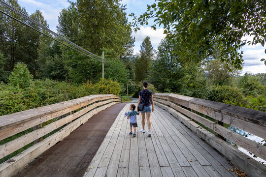 Mother And Child Walking On Wooden Bridge Through Forest At Great Blue Heron Nature Reserve, Chilliwack