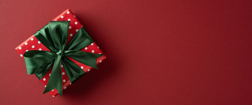 Red polka dot present with green satin bow for Merry Christmas and Happy New Year celebration ob banner maroon backdrop
