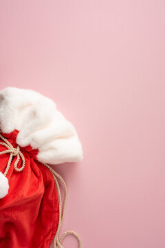 Merry Christmas red Santa sack with white fur trim holding a present for Happy New Year on pastel pink background
