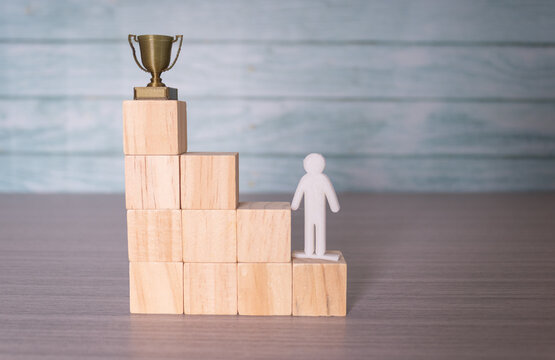 Step-by-step career progression concept, wooden blocks staircase with figure reaching for trophy
