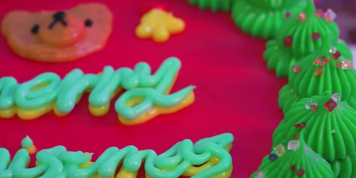 A macro, high-angle close-up shot focusing on a hilarious baking blunder where "Merry Christmas" is misspelled as "Merry Chrismus" with blue and yellow icing. The colorful custom cake features a vibra