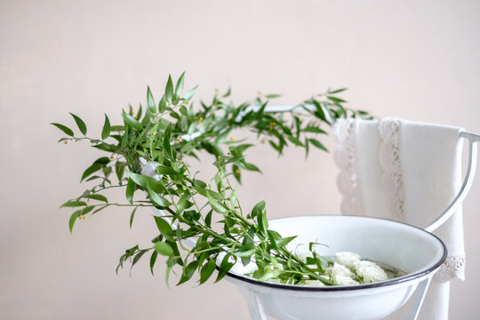 White roses and green foliage in a  metal bowl on a stand with a towel