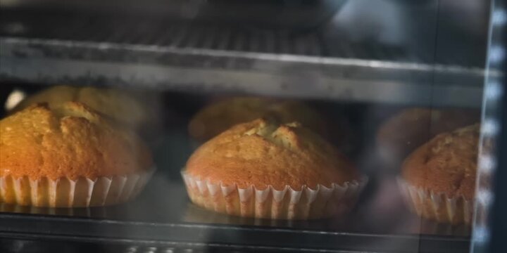 close-up shot capturing a tray of golden brown muffins baking inside a hot oven. The camera focuses on the rising, fluffy texture and the slightly crisp tops of the pastries as they bake to perfection