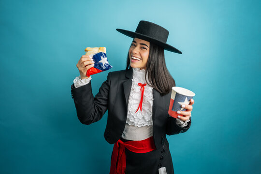 Chilean woman smiling wearing traditional national costume while holding an empanada and a drink cup with the national flag