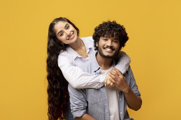 Obraz premium Joyful Smiling Young Mixed Race Couple Embracing Each Other With Love And Affection, Standing Together In Studio Against Bright Yellow Background. Relationship Concept.