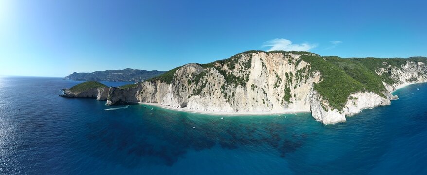 Aerial 180‑degree panoramic shot showing turquoise sea and white cliffs at Chomi Beach in Corfu near Paleokastritsa