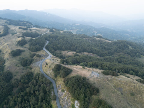 Aerial view of Parco Nazionale dell'Appennino Tosco-Emiliano featuring a winding mountain road, dense forests, and a solitary stone building in Provincia di Massa e Carrara, Italy.
