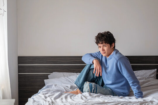 Tired teenage boy sitting on a bed with an apathetic look