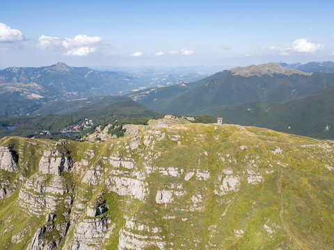 Aerial view of Parco Nazionale dell'Appennino Tosco-Emiliano with rocky mountain peaks, lush green slopes, and a distant lake in Provincia di Massa e Carrara, Italy.