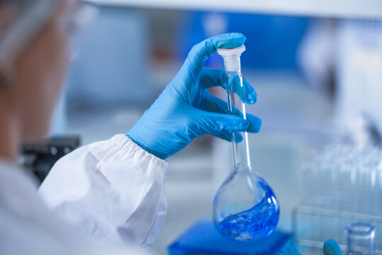 Gloved hands of a laboratory researcher swirling solution around the flask bulb in a contemporary biomedical research facility, in a clean and modern laboratory.