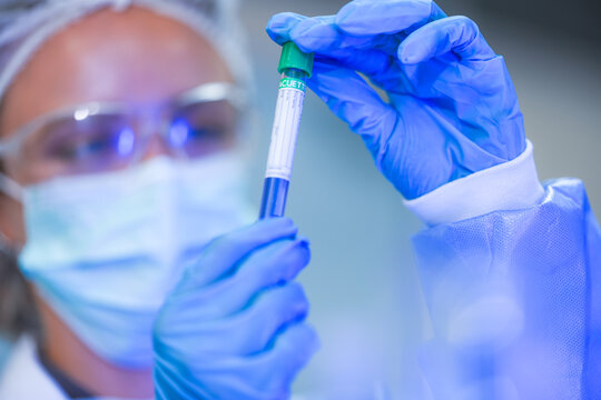 A young female lab scientist in white laboratory clothing, safety glasses and blue gloves gripping cap ready to twist it open in a modern medical research laboratory.