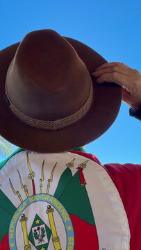 Holding a hat on their head and the flag of Rio Grande do Sul (southern Brazil) across their chest, amidst nature and under a blue sky. Tradition, freedom, and pride in being *ga&uacute;cho*. Farroupilha Wee