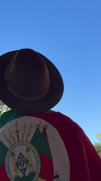Holding a hat on their head and the flag of Rio Grande do Sul (southern Brazil) across their chest, amidst nature and under a blue sky. Tradition, freedom, and pride in being *ga&uacute;cho*. Farroupilha Wee