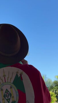 Holding a hat on their head and the flag of Rio Grande do Sul (southern Brazil) across their chest, amidst nature and under a blue sky. Tradition, freedom, and pride in being *ga&uacute;cho*. Farroupilha Wee