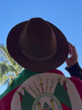 Holding a hat on their head and the flag of Rio Grande do Sul (southern Brazil) across their chest, amidst nature and under a blue sky. Tradition, freedom, and pride in being *ga&uacute;cho*. Farroupilha Wee