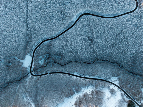 Aerial view of the Parco Nazionale dell'Appennino Tosco-Emiliano featuring a winding road cutting through a dense, snow-covered forest in Sassalbo, Provincia di Massa e Carrara, Italy.